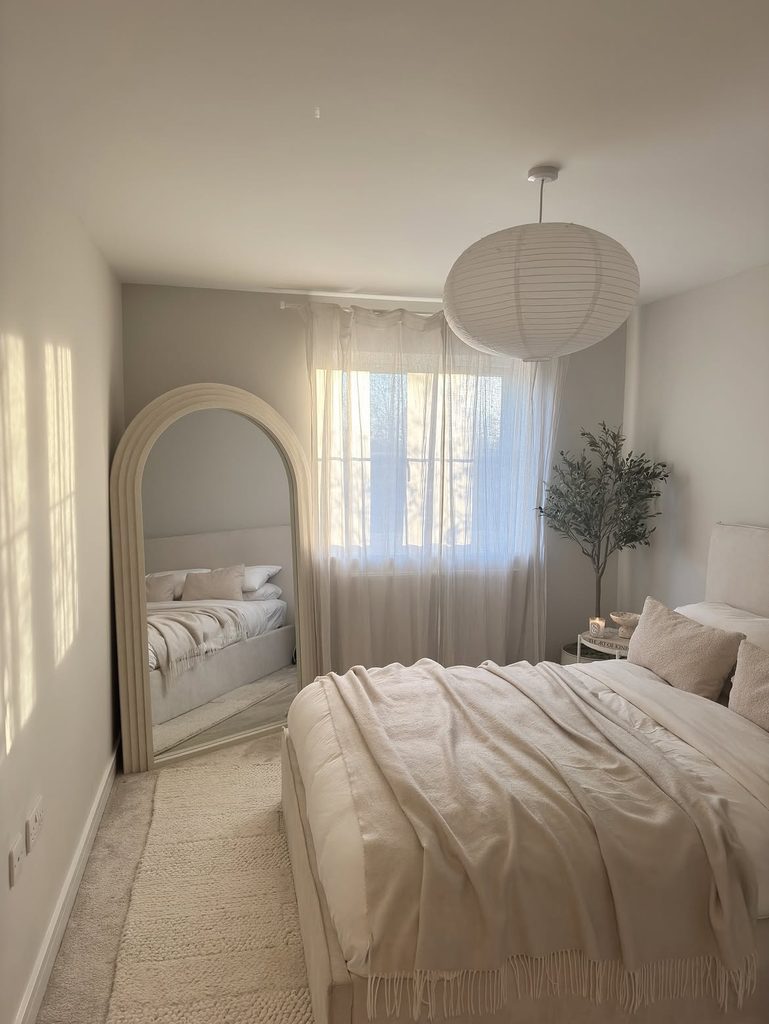 Neutral bedroom with arched floor mirror, sheer curtains, and paper globe pendant light