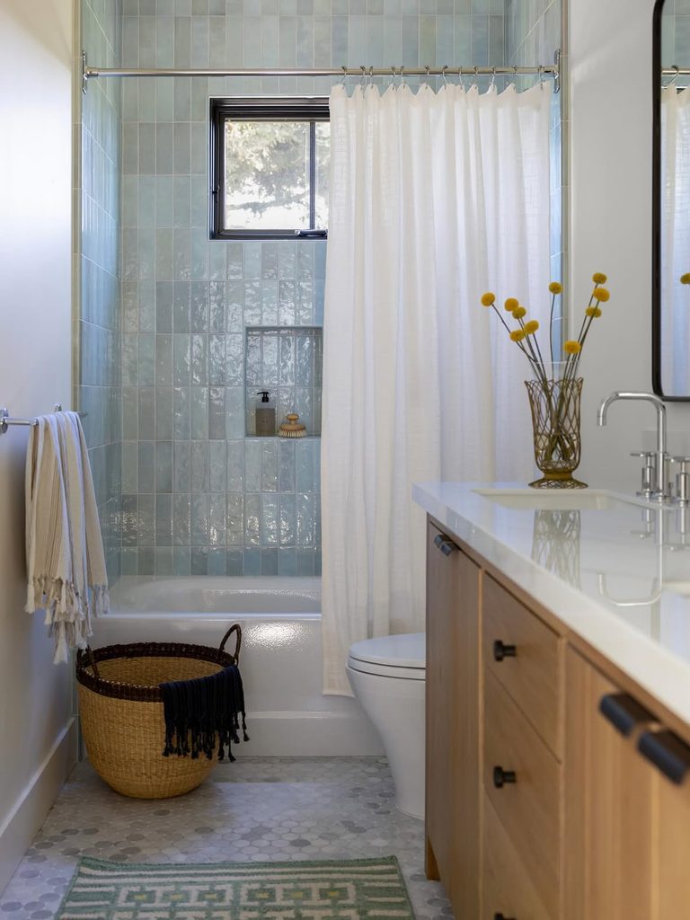 Blue bathroom ideas with aqua zellige tub surround, white linen curtain, and light oak vanity