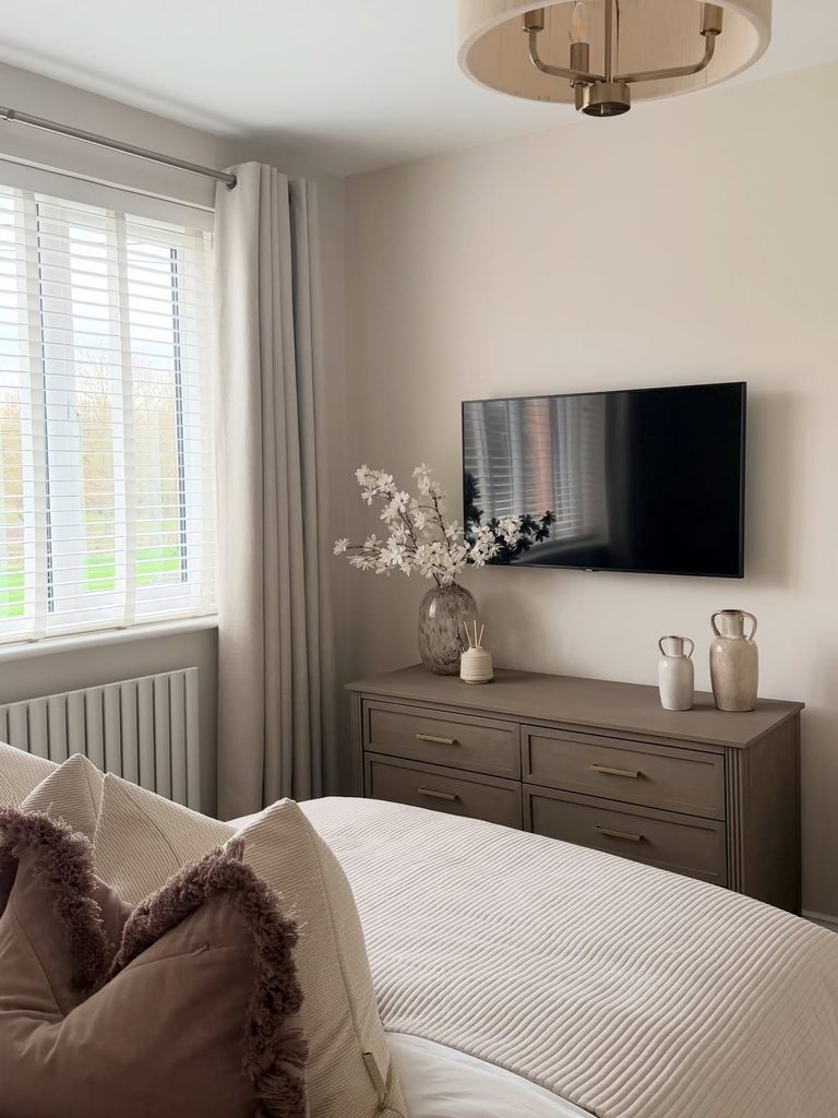 Neutral bedroom with dark taupe chest of drawers, wall-mounted TV, and faux blossom arrangement