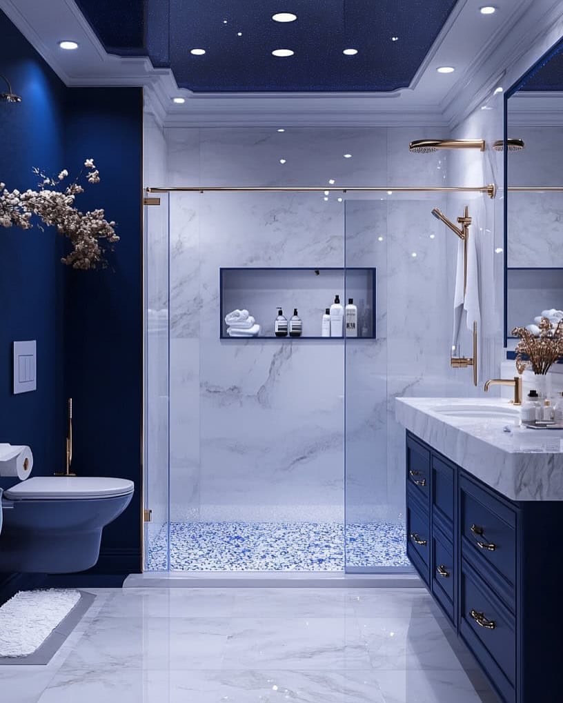 Luxury blue bathroom with marble shower walls, navy vanity, and brushed brass fixtures