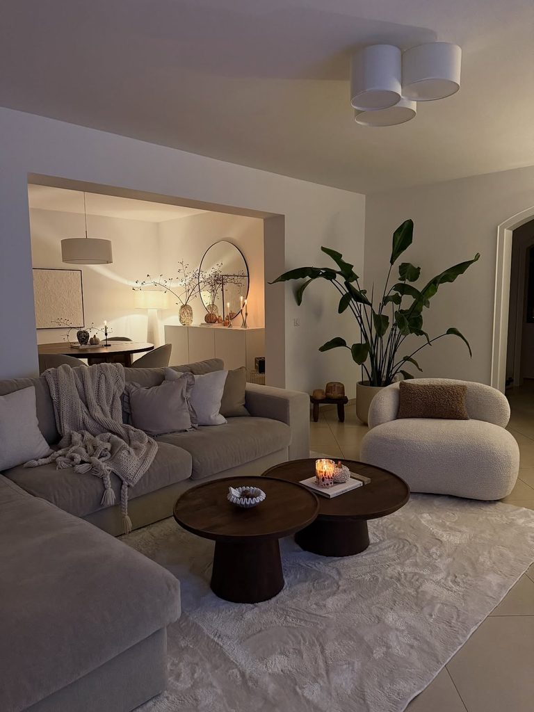 
Candlelit living room with boucle armchair large tropical plant and round walnut coffee tables