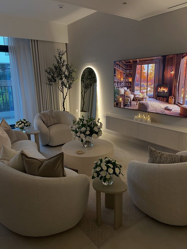 
Neutral living room with curved boucle armchairs white roses and arched backlit mirror